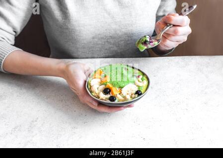 Gesunde Frühstücksschüssel. Grüner Smoothie, Granola, Nüsse und Früchte in Keramikschale in weiblichen Händen. Sauber essen, nähren, detox, vegetarisch, veg Stockfoto