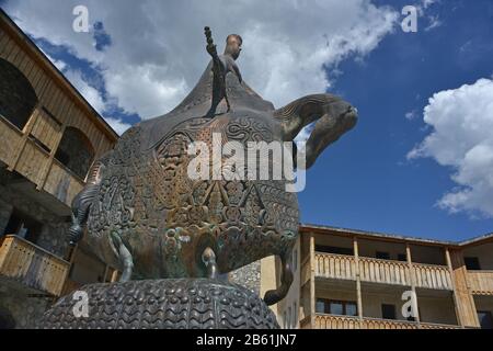 Denkmal der Königin Tamar in Mestia (Svaneti) vor Himmelshintergrund. Holzschlichte Gebäude sind mit Skulpturen umgeben. Stockfoto