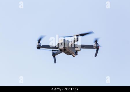 Ein schöner moderner schwarzer Drohnen-Quadrocopter mit dem Foto und einer Videokamera auf dem Brett fliegt gegen den blauen Himmel Stockfoto