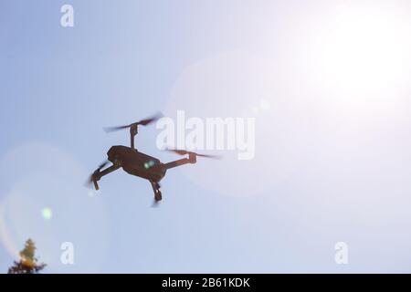 Ein schöner moderner schwarzer Drohnen-Quadrocopter mit dem Foto und einer Videokamera auf dem Brett fliegt gegen den blauen Himmel Stockfoto