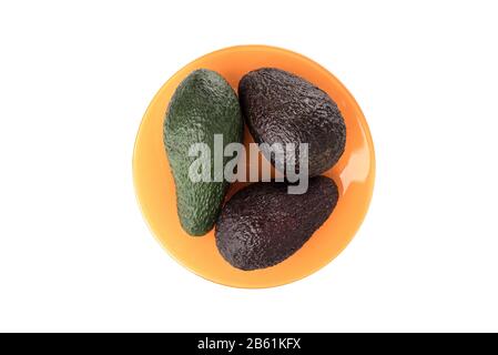 Avocado-Früchte auf einer orangefarbenen Platte über weißem Hintergrund. Tropische Früchte, die eine große Anzahl von Spurenelementen und Makrozellen enthalten. Kopierbereich. Stockfoto