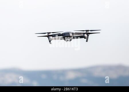 Ein schöner moderner schwarzer Drohnen-Quadrocopter mit dem Foto und einer Videokamera auf dem Brett fliegt gegen den blauen Himmel Stockfoto