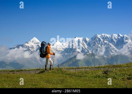 Frau (Backpacker) vor Bergen mit Schneehintergrund. Touristen liegt auf der Alpenwiese. Die Tviber-Halterung befindet sich im linken Teil des Bildes. Stockfoto