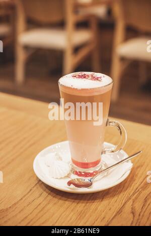 Latte Macchiato mit Kakaopulver und Kaffeebohnen auf Holzhintergrund.Latte in Glastasse. Große Tasse Cappuccino.Kaffee Mokka auf dem Holzschreibtisch Stockfoto