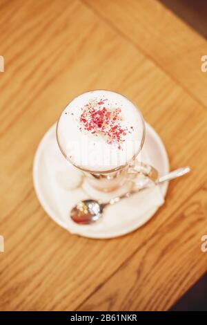 Latte Macchiato mit Kakaopulver und Kaffeebohnen auf Holzhintergrund.Latte in Glastasse. Große Tasse Cappuccino.Kaffee Mokka auf dem Holzschreibtisch Stockfoto