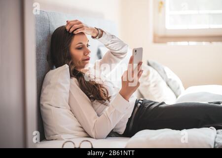 Besorgte Geschäftsfrau auf Geschäftsreise im Hotelzimmer und mit Smartphone. Stockfoto