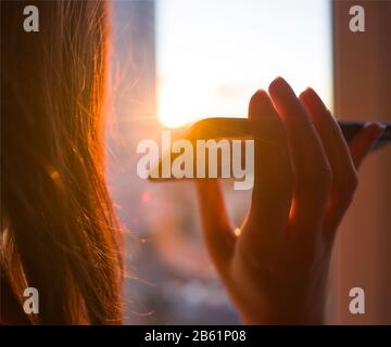 Das Mädchen hält ein Smartphone in der Hand, vor dem Hintergrund des sonnigen Sonnenuntergangs. Konzept Telefonanwendung für Menschen mit Behinderungen, Behinderte, Blinde Stockfoto