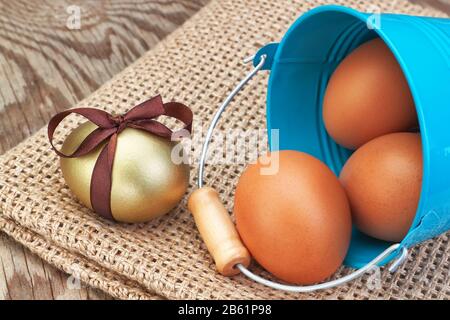 Blauer Eimer und goldene Ostereier auf einem Sacktuch verstreut. Stockfoto