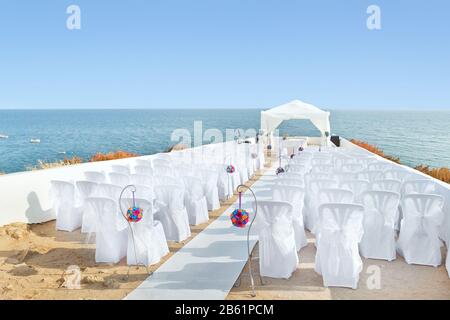 Ein wunderbarer Ort in den Dekorationen und Blumen für die Hochzeitsfeier. Mit weißen Stühlen am Meer. Stockfoto