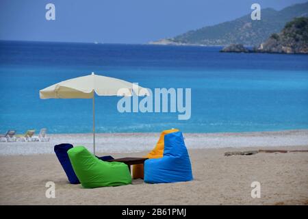 Platz zum Entspannen am Sandstrand. Mehrfarbige Sitze, die wie ein Sessel aussehen, umgeben kleinen Holztisch, weißer Sonnenschutz schützt vor Sonne. Stockfoto