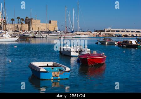 Bari, ITALIEN - 16. FEBRUAR 2020: Rustikale Boote im Fischerhafen vor dem Hintergrund moderner Jachten und des Castello Svevo in Bari, Apulien Stockfoto