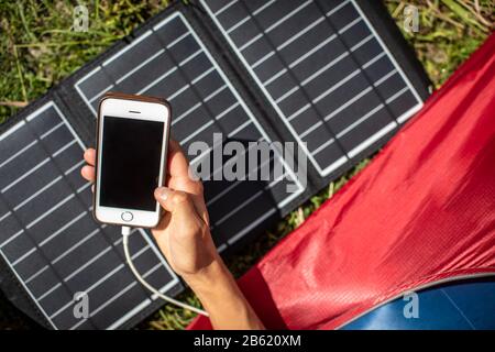 Handy wird während einer Fahrt im Freien mit einem Solarladegerät in einem Zelt aufgeladen Stockfoto