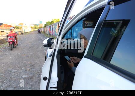 Makassar, Süd-Sulawesi, Indonesien. März 2020. Eine Frau, die einen Hijab trägt, entspannt sich in ihrem Auto, während sie ein Handy hält. Diese Frau kam, um die nachmittägliche Atmosphäre rund um Losari Beach, Makassar City, South Sulawesi Provinz, Indonesien zu genießen. Gutschrift: Herwin Bahar/ZUMA Wire/Alamy Live News Stockfoto