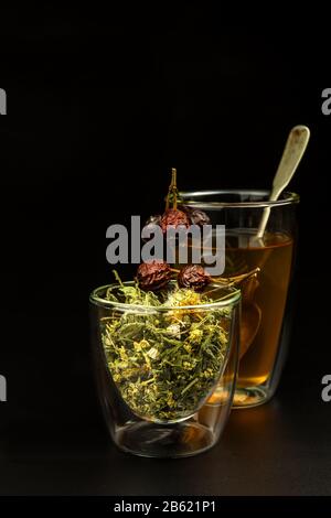 Tasse Kräutertee. Verschiedene Kräutertezutaten in Glasgefäßen über schwarzem Hintergrund. Traditionelle Medizin gegen Grippe und Kälte. Stockfoto