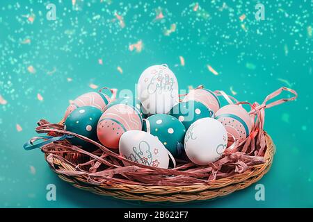 Farbige verzierte Eier auf Strohtablett auf neominzem Hintergrund mit fliegenden Saiten. Osterkonzept. Stockfoto