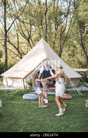 Glückliche Familie: Mutter, Vater, zwei Kinder Töchter auf der Natur bei Sonnenuntergang, Tanz und Spaß. Boho-Stil, wigwam auf dem Hintergrund Stockfoto