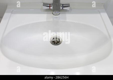 Weißes Keramikwaschbecken mit ovaler Schüssel, Ablass und grauem Hahn aus Edelstahl. Stockfoto