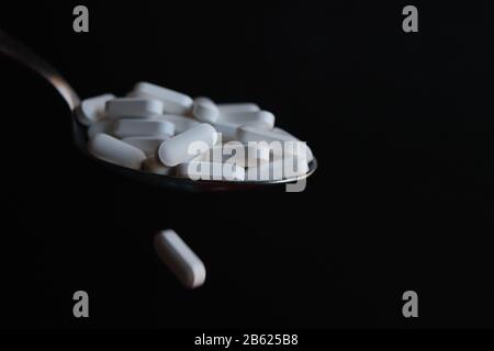 Weiße Pillen aus Löffel gegossen wie flüssige Medikamente mit schwarzem Hintergrund Stockfoto