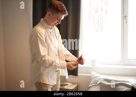 Attraktive schöne, hübsche, weiße Hemden, Kerl, der sich auf ein Datum, eine Hochzeit, ein wichtiges Ereignis, ein Nah-Seitenansicht-Foto vorbereitet. Morgen. Mann, der zur Arbeit geht, Stockfoto