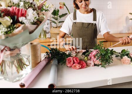 Blumenfrau schafft einen Blumenstrauß mit Band am Tisch Stockfoto