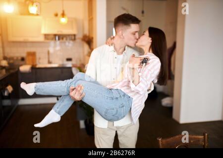 Konzentrieren Sie sich auf neue Schlüssel des neuen Hauses, Männer und Frauen, die sich in ihrer neuen Wohnung küssen. Nahaufnahme Foto. Liebe, Beziehung. Verschwommener Hintergrund Stockfoto