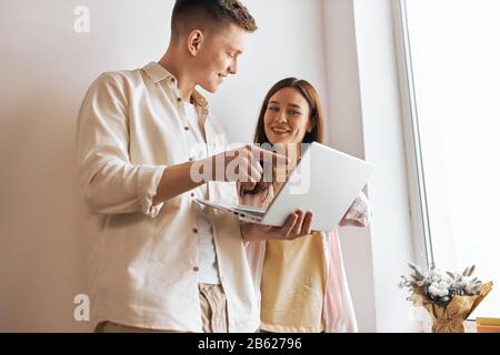 Junger, gut aussehender Programmierer, der den Computer der Frau repariert, Mann, der Frau hilft, mit dem Laptop zu arbeiten, Nahaufnahme Foto. Mann zeigt auf den Bildschirm Stockfoto