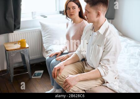 Verzweifelte Ehepaare, die am Rand des Bettes sitzen und zwischen den beiden versticht sind. Seitenansicht schließen Foto.beleidigendes Paar, das jeden OTH betrachtet Stockfoto