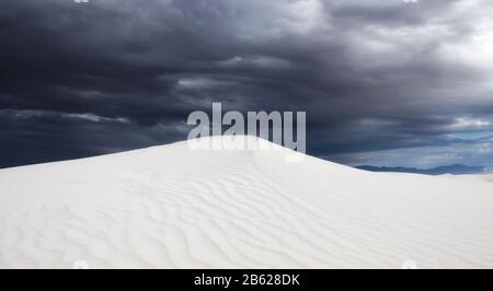 Sturm nähert sich einer Sanddüne im White Sands National Park, NM. Textur in Sicht unter den stürmischen Wolken. Stockfoto