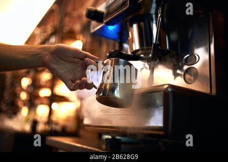 Der männliche Barkeeper ist am Arbeitsplatz. Der Mann macht Kaffee mit einer Kaffeemaschine. Cappuccino, Shop, der Barkeeper Stockfoto