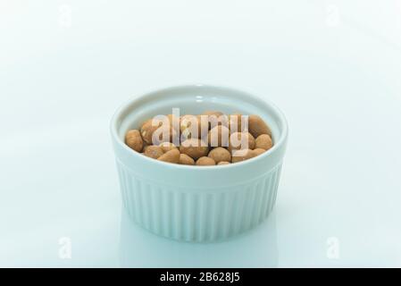 Geröstete Erdnüsse aus salzhaltiger Farbe auf weißem Hintergrund mit Kopierraum. Japanische Erdnüsse in einer weißen Keramikschale auf einem weißen Tisch. Selektiver Fokus. Stockfoto