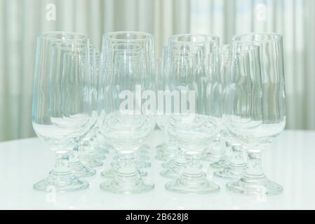 Leere Kristallgläser nebeneinander auf weißem Tisch. Sammlung verschiedener Gläser für Wasser und Saft isoliert auf weißer Vorderansicht. Leere Brille. Stockfoto