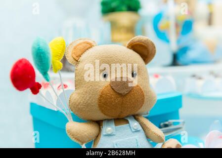 Junge Partydekoration mit Teddybären, die bunte Luftballons neben luxuriöser blauer Keramikvase mit verschwommenem Hintergrund hält. Stockfoto