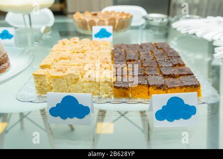 Tablett mit zwei selbstgemachten Kuchen von Hand. Karottenkuchen mit Schokolade und Cornmeal Kuchen auf Glastisch. Kuchen in eckige Stücke geschnitten. Stockfoto