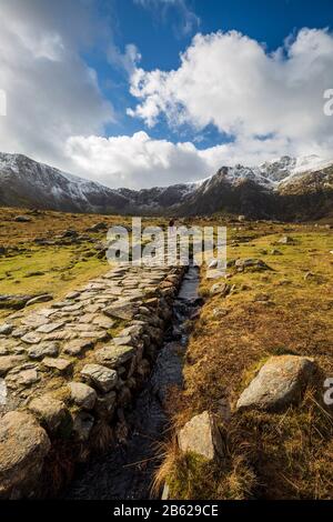 Der Steinweg, der zum Lake Idwal führt, und die schneebedeckten Berge von Snowdonia, Wales Stockfoto