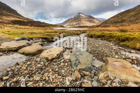 Stepping Stones über Schmelzwasser von schneebedecktem Glyder Fawr, das nach Llyn Idwal führt, mit Pen yr Ole Wen im Hintergrund, Snowdonia, Nordwales Stockfoto