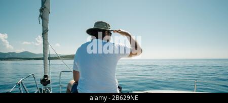 Mann, der auf den Schiffen sitzt, beugt sich und genießt die Jachtreise. Segel-, Segelsport- und Reisekonzept. Stockfoto