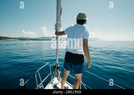 Mann, der auf den Schiffen steht, beugt sich und genießt die Jachtreise. Segel-, Segelsport- und Reisekonzept. Stockfoto