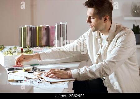 Junge hübsche, fair-haarige Achitect sitzt am Tabel und arbeitet an Projekt, Nahaufnahme Foto: Lifestyle, Hobby, Interesse Stockfoto