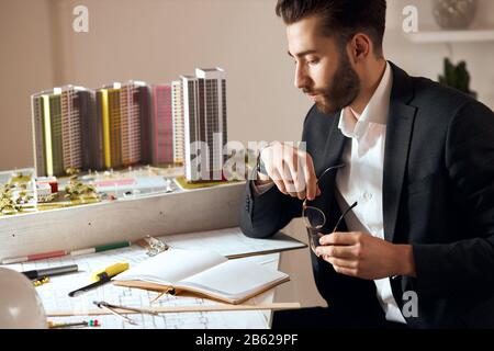 Seriöser, nachdenklicher Architekt, der ein Projekt aufstellt, während er am Schreibtisch am Arbeitsplatz sitzt. Nahansicht Foto: Rekonstruktion, Lebensstil, Beruf, Beruf, Stockfoto