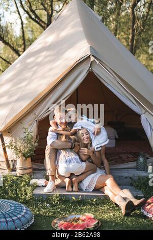 Fantastischer Familientag, Picknick und Camping. Glückliche Familie, Mutter, Vater und zwei Töchter, die in einem großen Boho-Zelt sitzen und lächeln und sich umarmen Stockfoto