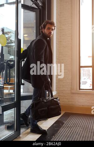 Der junge gutaussehende Geschäftsmann hat die Arbeit verlassen und das Büro verlassen, der Mann schließt die Tür und geht nach Hause. Foto in voller Länge. Stockfoto