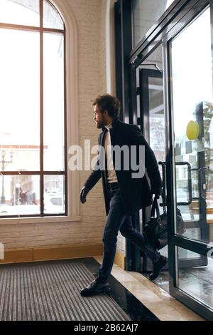 Stilvoller, gutaussehender Mann mit Tasche aus dem Gebäude, Foto in voller Länge. Einbrecher, der mit Geld, Verbrechen davonläuft, Mann eilt irgendwo hin, Mann schaut auf das w Stockfoto