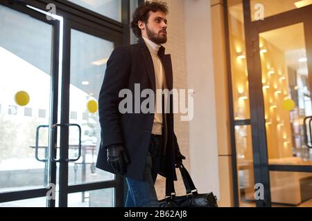 Ernster junger Mörder, der jemanden töten wird, ermordet in schwarzen Handschuhen, die einen Beutel halten und das Geschäft in die Luft sprengen wird, Menschen, Nahaufnahme Foto. Ter Stockfoto