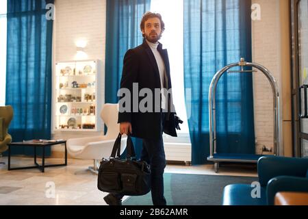 Bärtiger Mann, der im Saal des Hotels spaziert, Geschäftsreise, Urlaub, Urlaub, Nahaufnahme mit Seitenansicht. Stockfoto