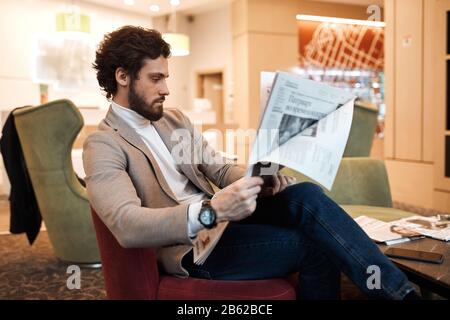 Kerl sitzt auf dem Sofa, hält Zeitung in den Händen, Wissen, Massenmedien, Nahansicht Foto Stockfoto