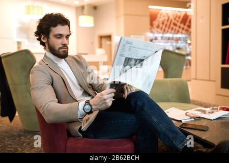 Junger attraktiver Mann in Mode Freizeit Kleidung, die sich im Warteraum ausruhen, auf einen Flug warten, einfarbiges, nahes Seitenbild. Stockfoto