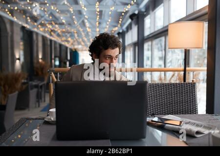 Der serriöse Kerl kann einige Probleme nicht lösen, indem er Passanten beobachtet, die auf der Straße spazieren gehen. Schließen Sie den auffälligen Kerl, der hinter dem Laptop sitzt Stockfoto