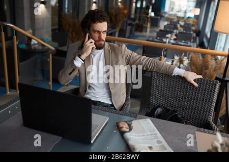 Ernster unglücklicher frostender Mann, der auf dem Stuhl sitzt und Gespräche führt, unangenehmes Gespräch mit dem Kunden, Frustration, negatives Gefühl und Emot Stockfoto