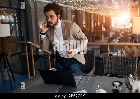 Junger eleganter Mann, der hinter dem Tisch steht und Kunden Waren anbietet, mit Freunden spricht und Geschäftsgespräche führt Stockfoto