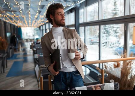 Fantastischer, angenehmer Mann mit Laptop, der auf einen Kunden wartet und einen Geschäftsplan aufstellt. Nahaufnahme Foto. Suche, Suche nach Inspiration, Seitenansicht Foto Stockfoto